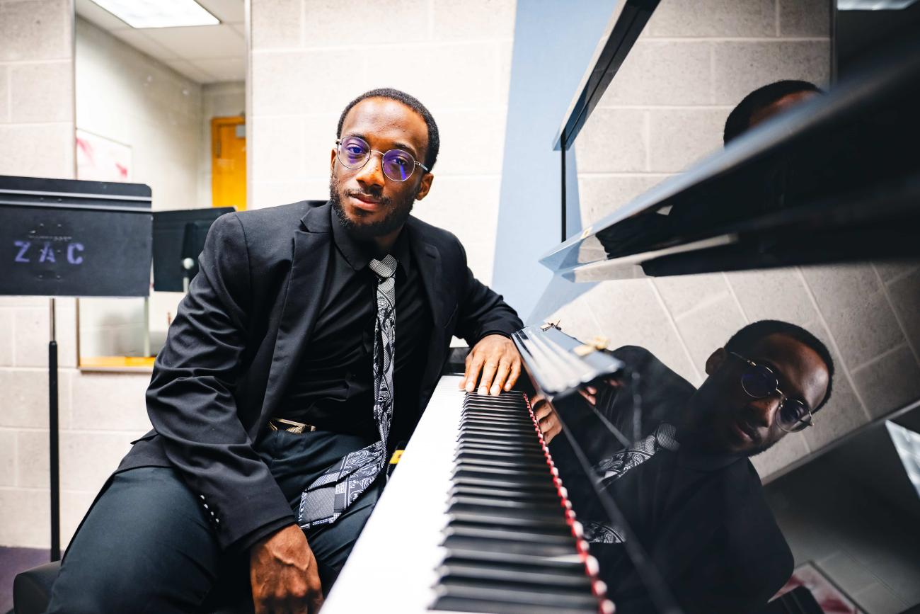 Loba Salami sits at a piano wearing a black suit and tie.
